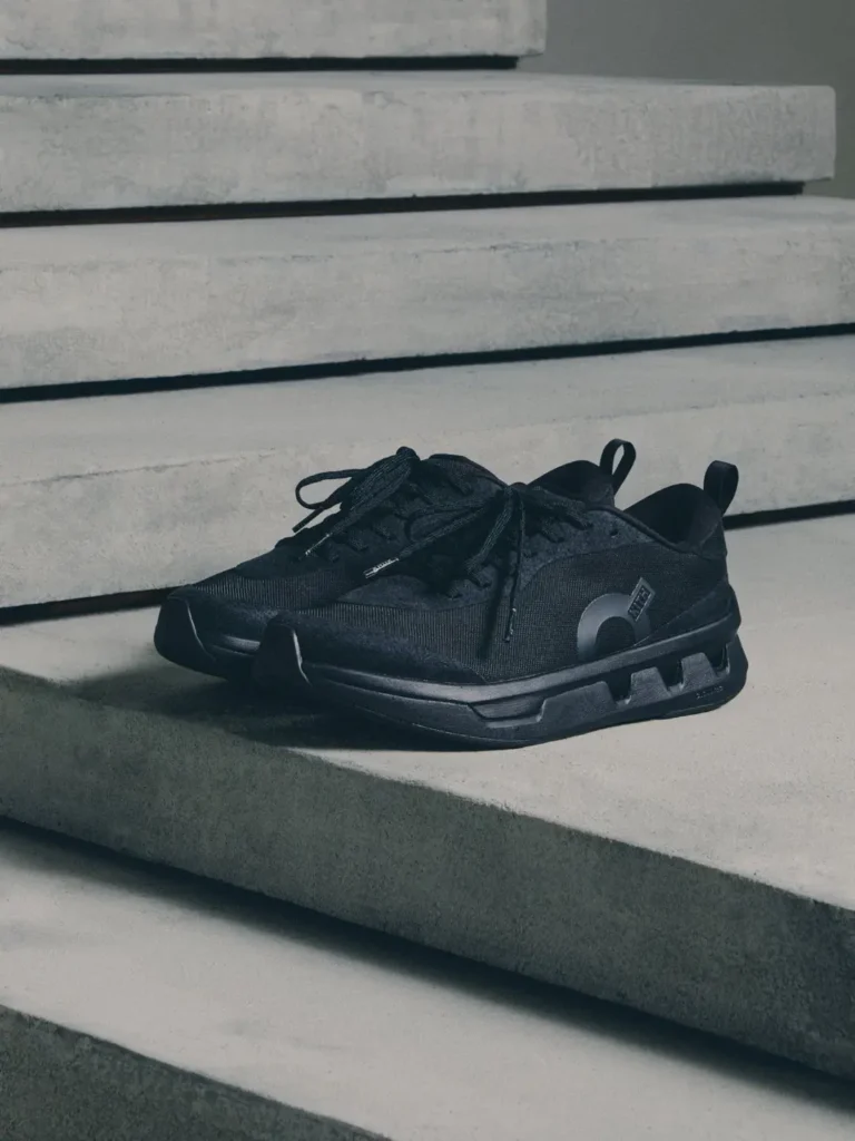 Black athletic sneaker with mesh upper, tied laces and thick segmented sole on concrete steps