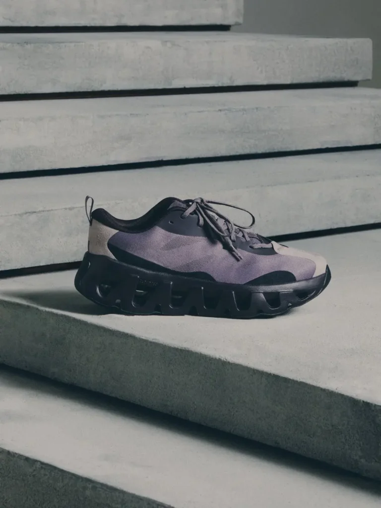 Gray-purple athletic shoe with black laces and chunky sculpted sole resting on concrete steps
