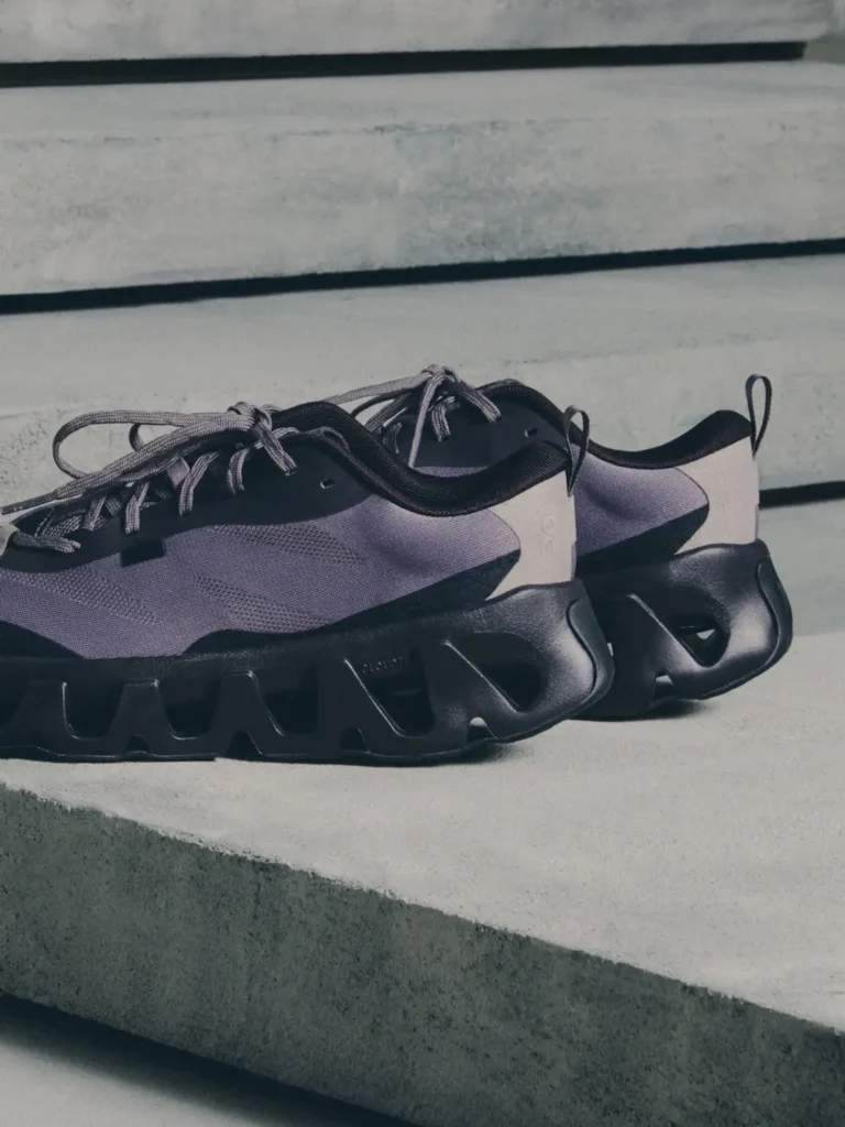 Pair of purple knit sneakers with black laces and oversized sculptural black foam soles on concrete steps