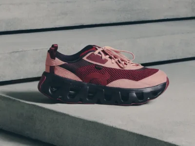 Pink and burgundy athletic sneaker with mesh panels and chunky black sole resting on concrete steps