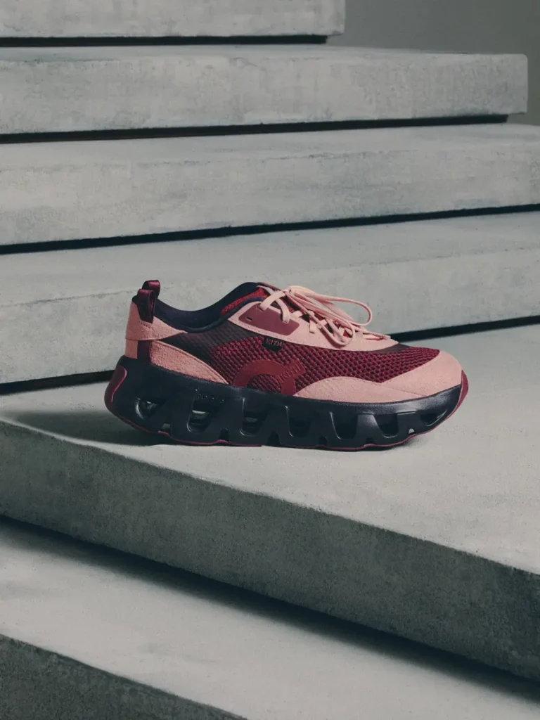 Pink and burgundy athletic sneaker with mesh panels and chunky black sole resting on concrete steps