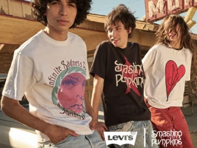 Three people in graphic Smashing Pumpkins T-shirts stand beside a vintage car outside a motel sign
