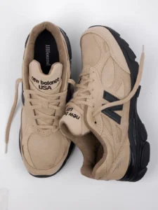 Pair of beige New Balance sneakers with black soles and oversized side logos, arranged on a white background