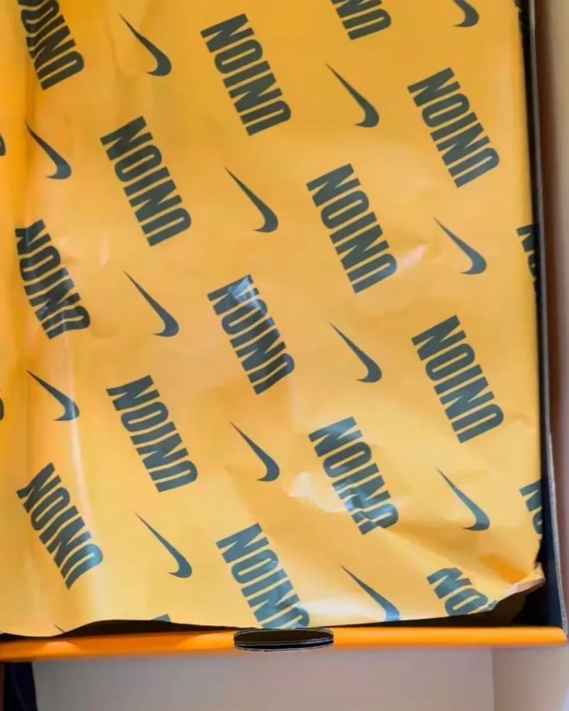Yellow Nike-patterned tissue paper draped over an open box, with repeated black logos and a visible center flap lip