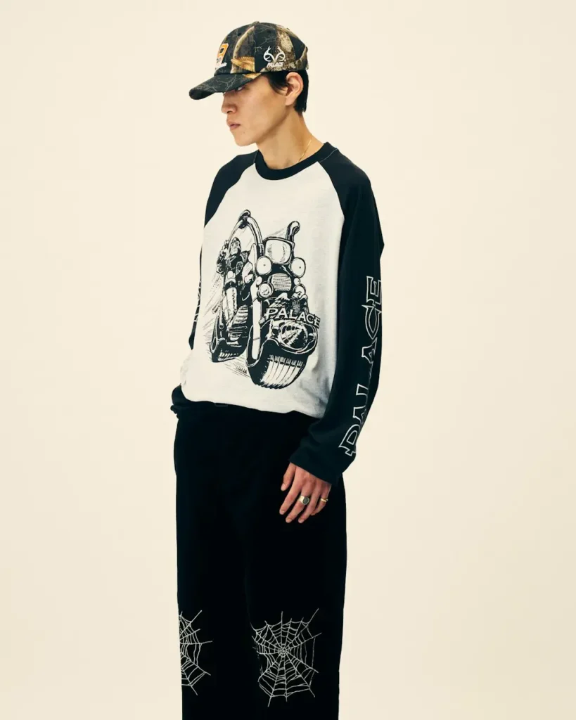 Person in profile wearing a black cap, black-and-white graphic raglan shirt, and black pants with web designs at the knees