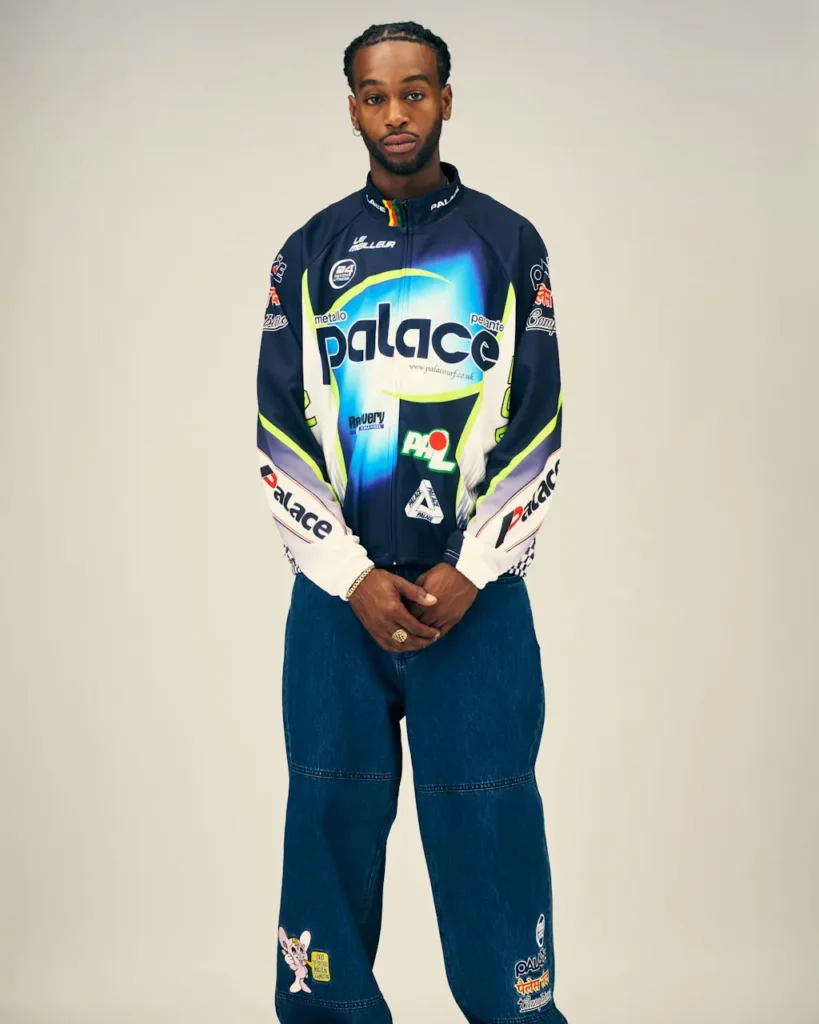 Person standing against a beige background in a navy Palace racing jersey with neon accents and wide-leg embroidered jeans