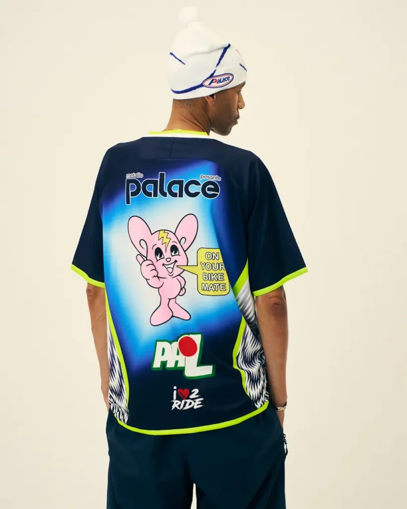 Person turned away wearing a white Palace beanie and navy cycling jersey with neon trim, cartoon graphic, and logos against