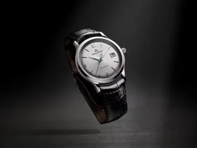 Jaeger-LeCoultre watch with a silver dial and black leather strap levitating above a dark reflective surface