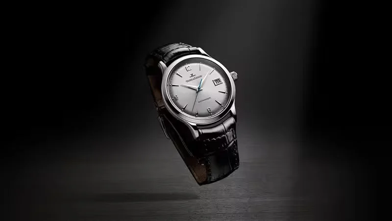 Jaeger-LeCoultre watch with a silver dial and black leather strap levitating above a dark reflective surface