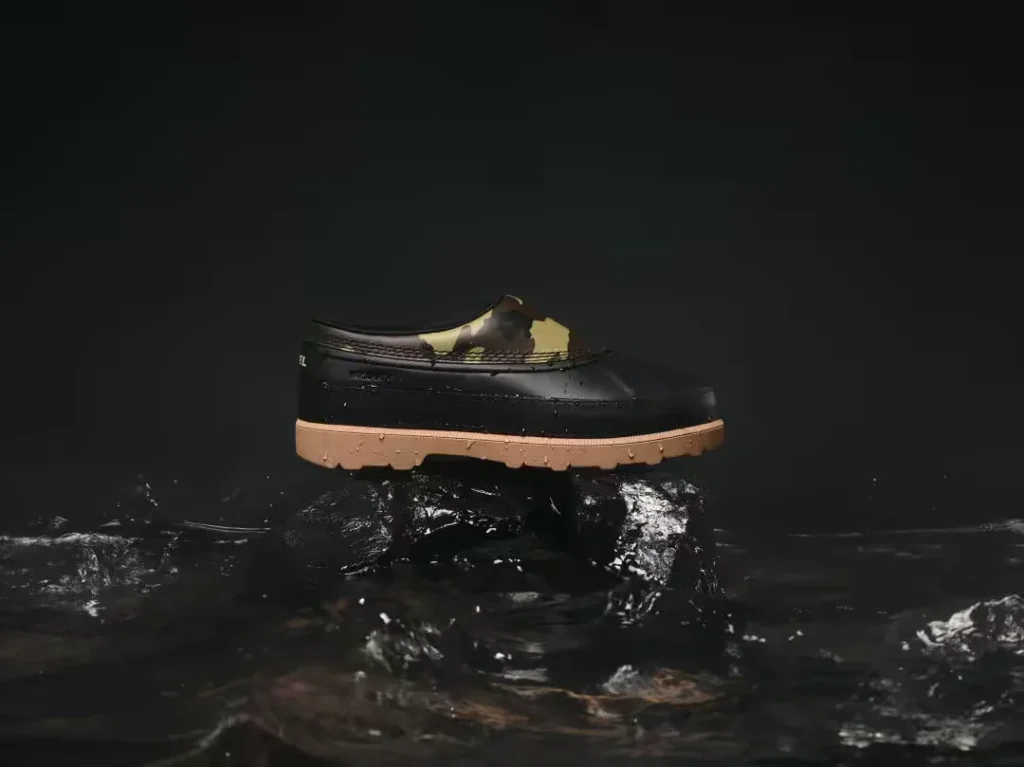 Black waterproof mule with tan lug sole and camouflage lining, perched on a rock amid dark rippling water