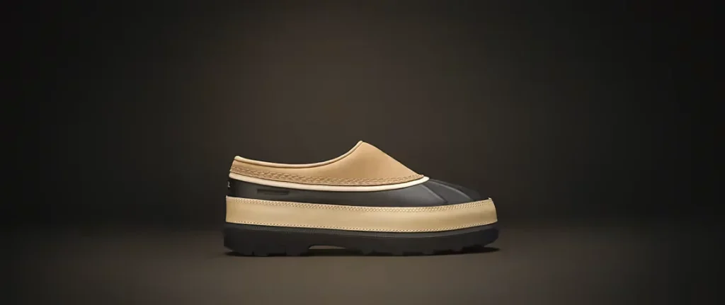 Beige and black waterproof mule with a moccasin-style upper and thick lugged sole on a dark background