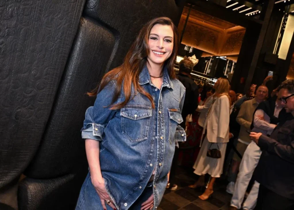 Anne Hathaway smiles in a blue denim shirt dress at a crowded Moncler store opening event