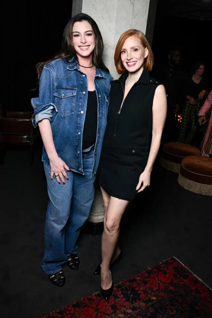 Anne Hathaway and Jessica Chastain pose together, wearing a denim outfit and a sleeveless black dress at an event