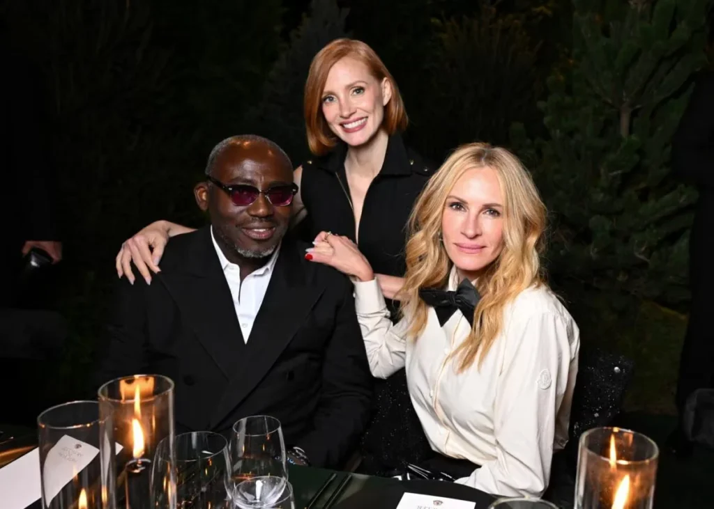 Julia Roberts poses with two guests at a candlelit dinner, wearing a white blouse with a black bow tie