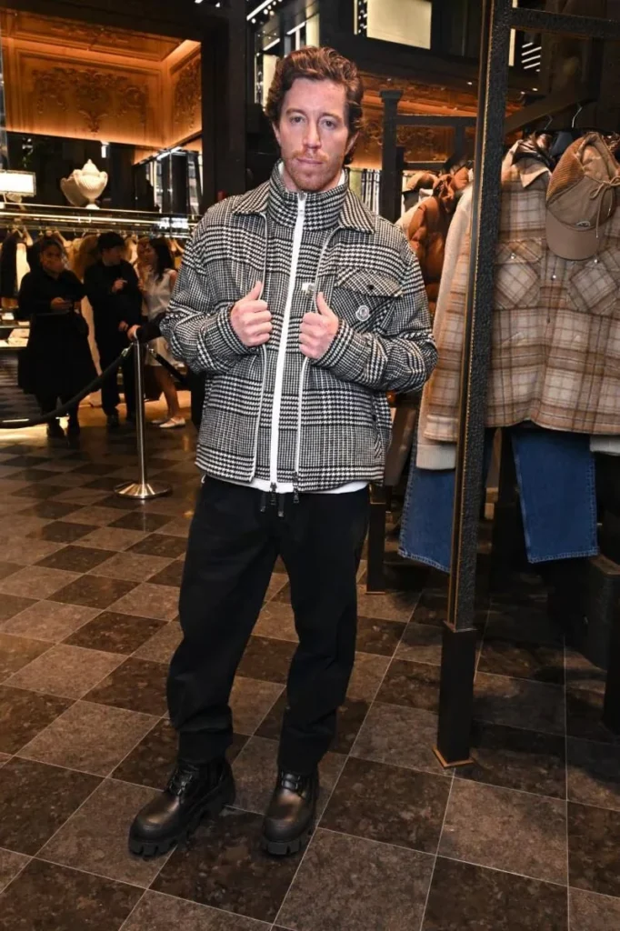 A man stands in a Moncler store wearing a black-and-white houndstooth jacket, black pants, and chunky boots