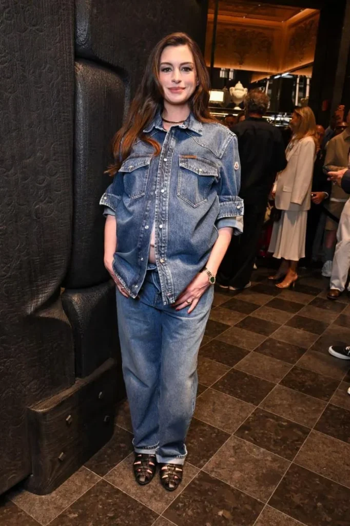 Anne Hathaway poses in a denim shirt and matching wide-leg jeans at a dimly lit Moncler event