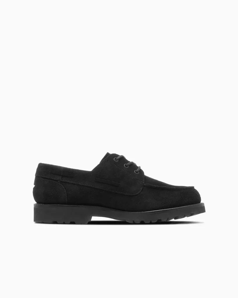 Black suede lace-up boat shoe with a moc-toe, raised heel, and lugged rubber sole on a white background