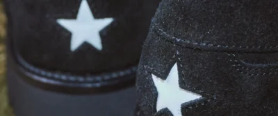 Close-up of black Converse sneakers featuring contrasting white star patches, with one shoe overlapping the other