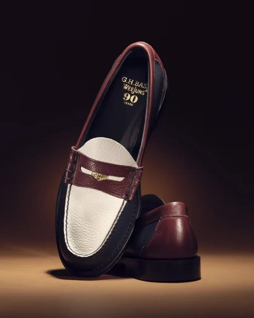 Two burgundy and black leather loafers with cream pebbled leather uppers, displayed on a warm surface against a dark