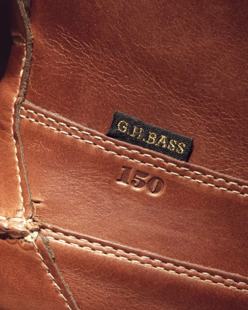 Close-up of brown leather with white stitching, embossed “150” marking and black G.H. Bass label