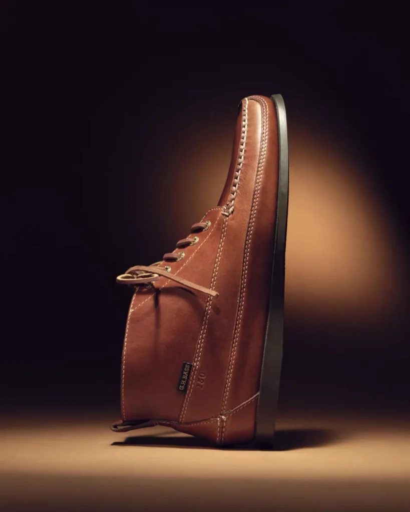 Brown leather high-top sneaker with contrast stitching and black sole, standing on a wood surface against a dark background