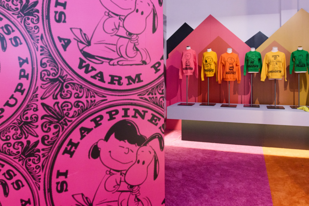 Snoopy and Peanuts sweatshirt designs displayed on mannequins against colorful geometric panels beside a pink printed wall