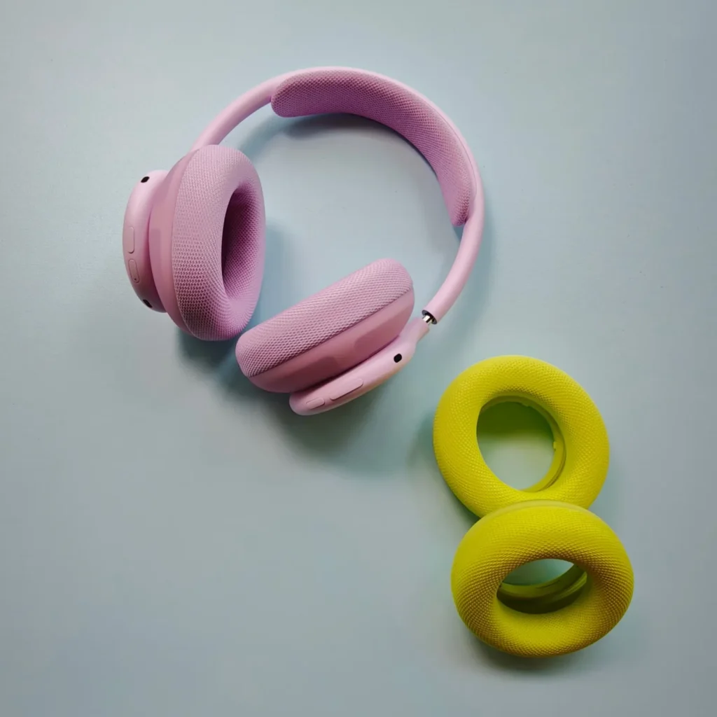 Pink over-ear headphones beside two yellow ring-shaped speakers on a pale blue surface