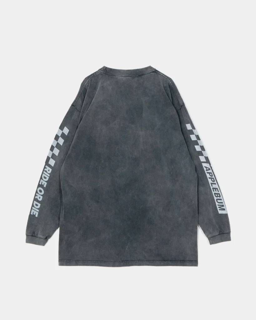 Back of a faded charcoal long-sleeve shirt with checkerboard sleeve stripes and APPLEBUM lettering on a light background