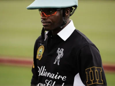 Black polo-wearing rider in a white and mint helmet with orange sunglasses on a blurred racetrack background