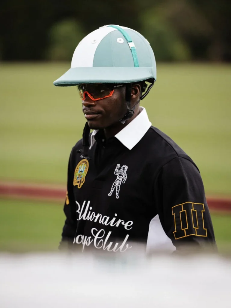 Black polo-wearing rider in a white and mint helmet with orange sunglasses on a blurred racetrack background