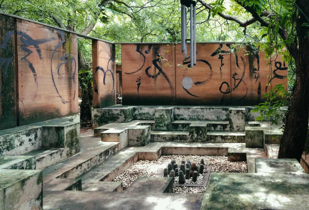 Moss-stained concrete amphitheater with stepped benches, white pebbles, dark stones, and graffiti walls beneath trees