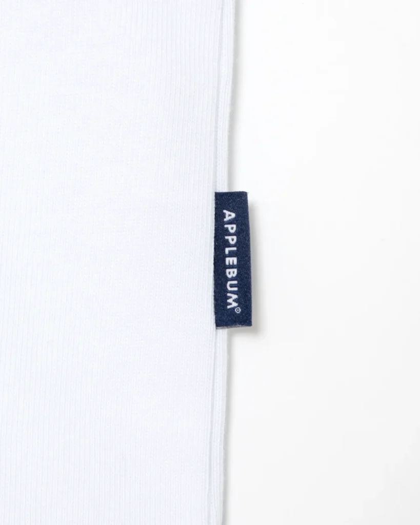 Close-up of white ribbed fabric with a navy APPLEBUM® label against a white background