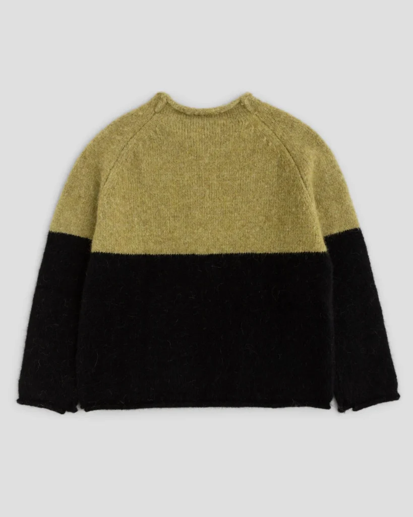 Mustard and black color-blocked wool sweater laid flat against a light gray background