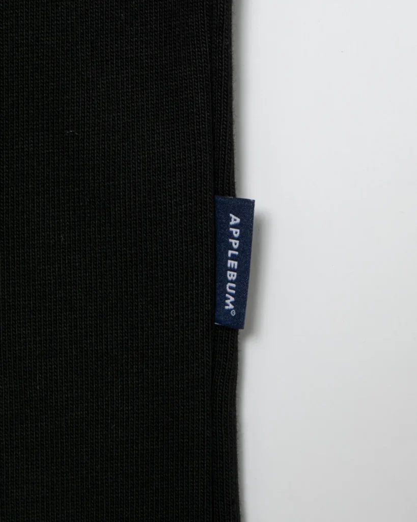 Close-up of black ribbed fabric with a navy APPLEBUM label against a white background