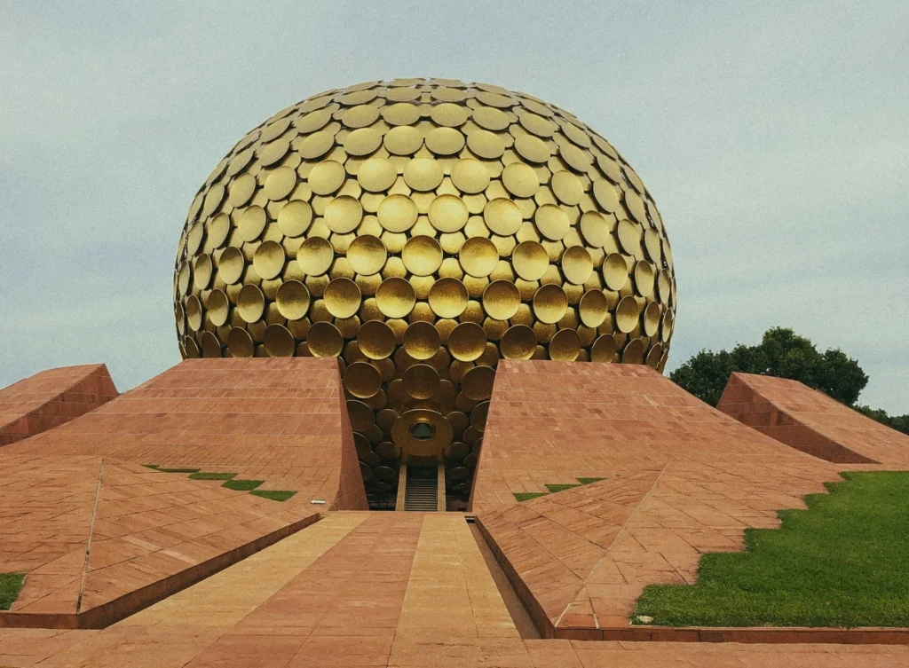 Golden spherical building covered in circular panels, rising behind terracotta geometric terraces and a central walkway