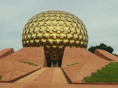 Golden spherical building covered in circular panels, rising behind terracotta geometric terraces and a central walkway