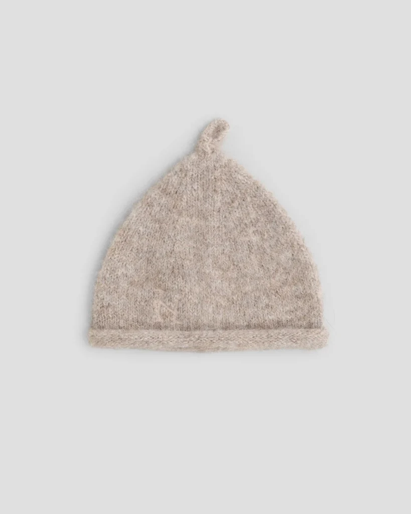 Beige fuzzy knit beanie with a folded brim and small loop at the crown on a light gray background