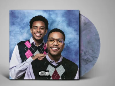 Anderson .Paak and Cordae pose together in argyle sweater vests, shown on a blue album cover beside a vinyl record