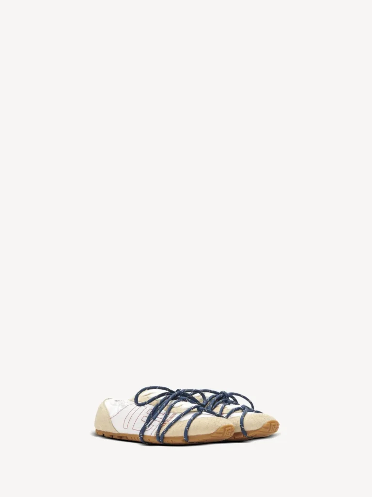 Pair of cream low-profile sneakers with navy rope laces and tan rubber soles on a white background