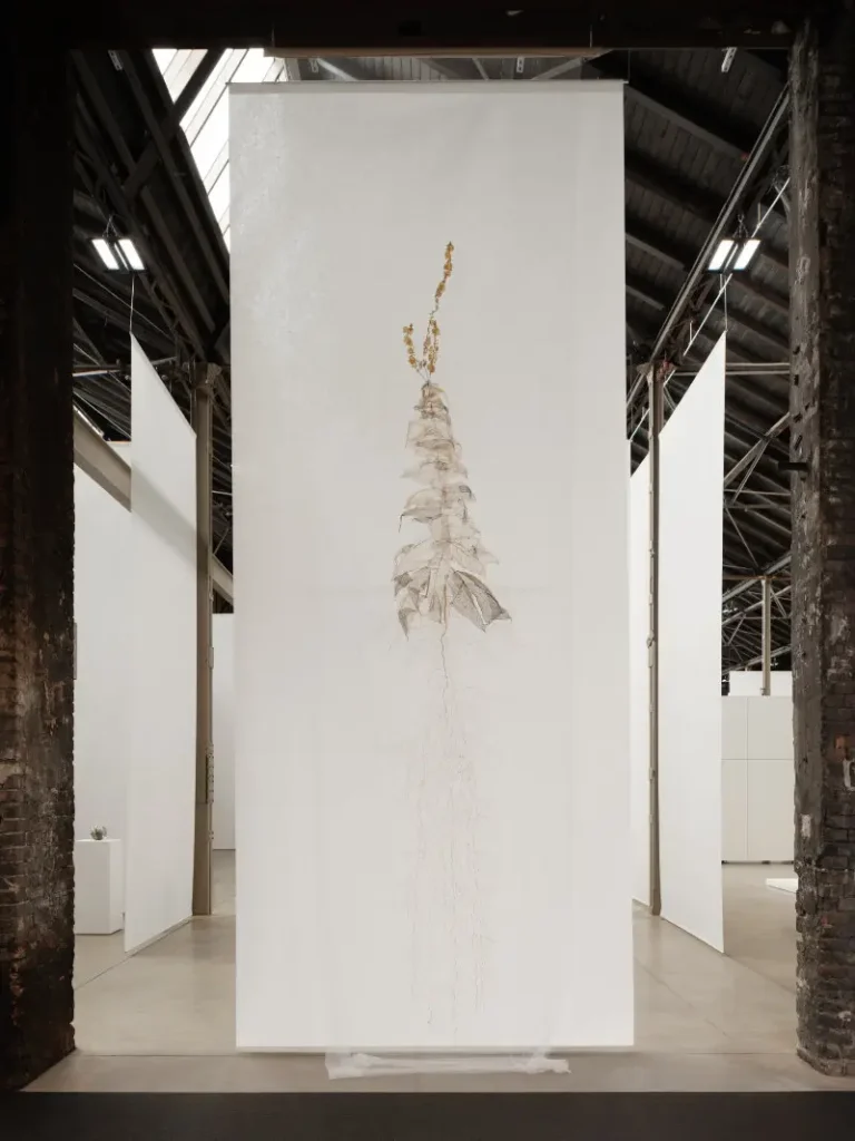 Tall white gallery panel displaying a delicate, faded botanical drawing with a brown-gold flower stem in an industrial