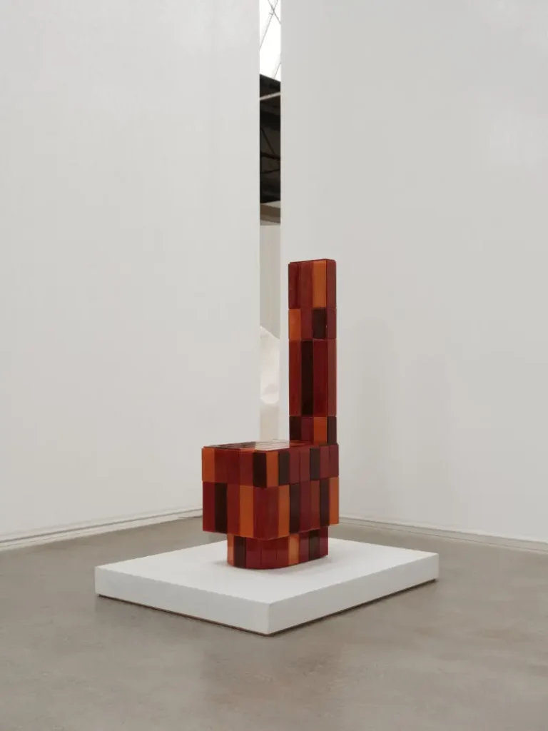 Red and amber translucent block sculpture resembling a chair, displayed on a white plinth in a gallery