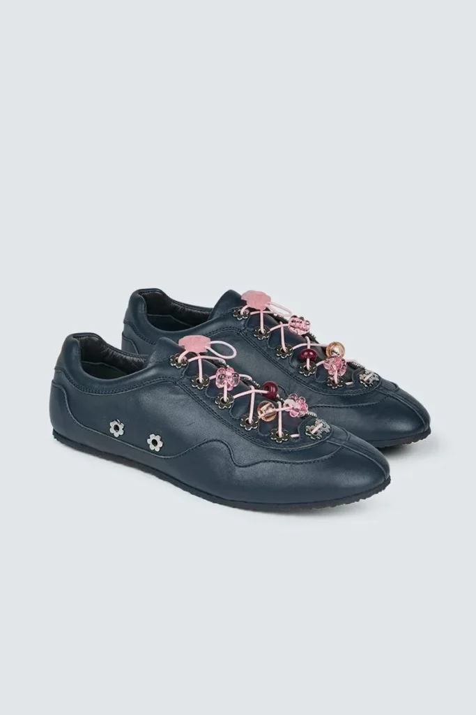 Pair of dark navy low-profile sneakers with pink laces, floral charms and small flower studs on a pale background