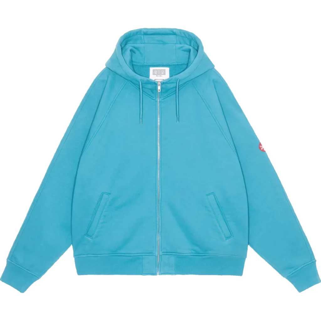 Turquoise zip-up hoodie with drawstring hood, slanted pockets, ribbed hem and a red sleeve patch on white background
