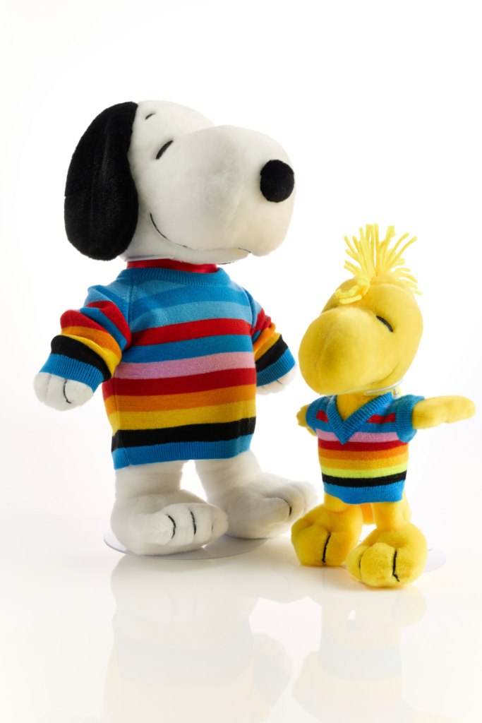 Plush Snoopy and Woodstock stand side by side in colorful striped sweaters against a white background