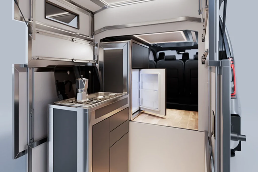 Camper van interior with a compact stainless-steel kitchenette, moka pot, open refrigerator, and rear passenger seats