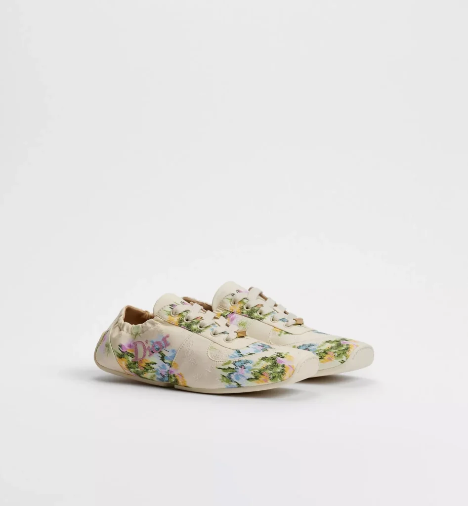 Pair of low-profile Dior sneakers with cream uppers, colorful floral-print panels, white laces, and flat soles on a white