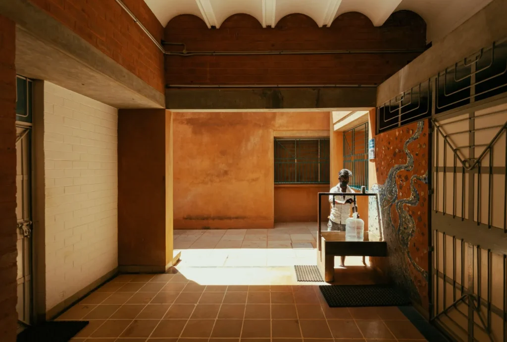Person standing behind a water dispenser in a terracotta-tiled corridor with arched ceiling and mosaic-covered wall