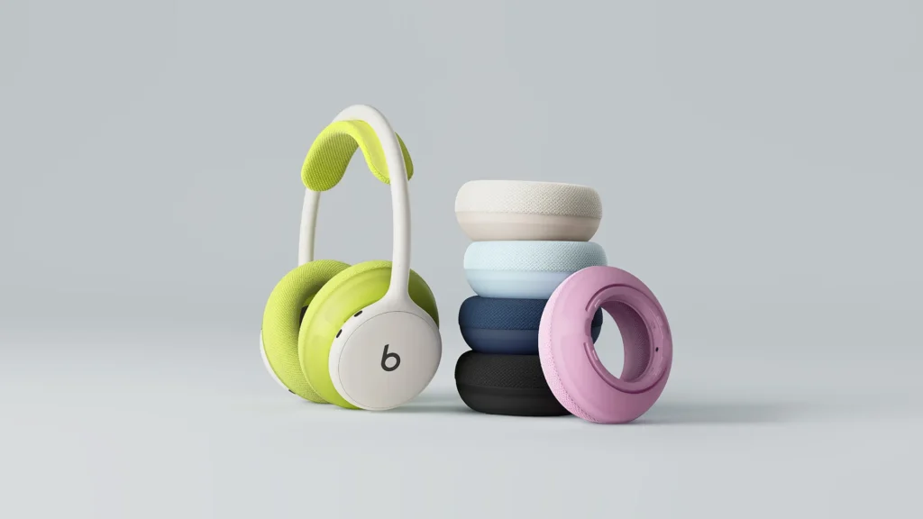 Lime-green and white Beats headphones beside a stack of pastel and dark fabric-covered earbuds on a gray background