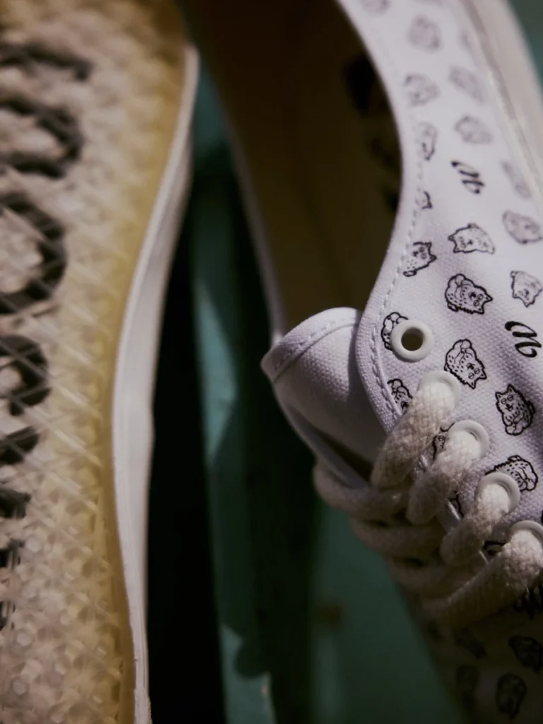 Close-up of white canvas sneakers with black cat illustrations and cream textured soles against a dark green background