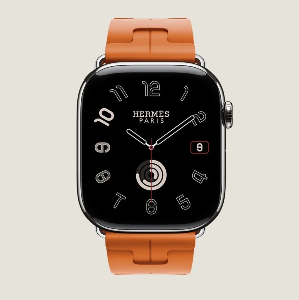 Hermès Apple Watch with orange leather band, black face, silver case, and white outlined numerals on a beige background